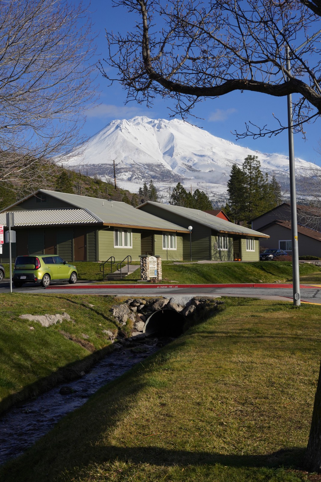 A snow-capped mountain beyond houses and a stream.